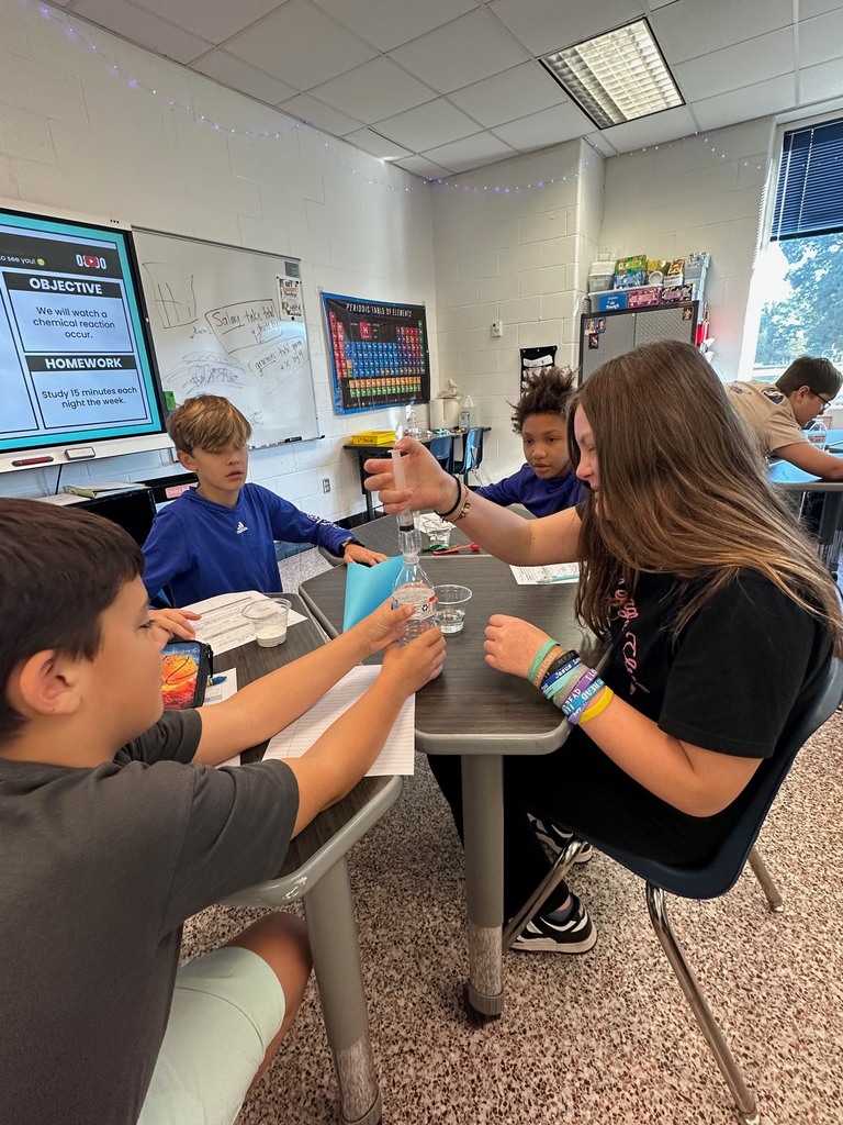 Two students work together during a science lab, observing a balloon inflate as a reaction occurs inside a bottle.