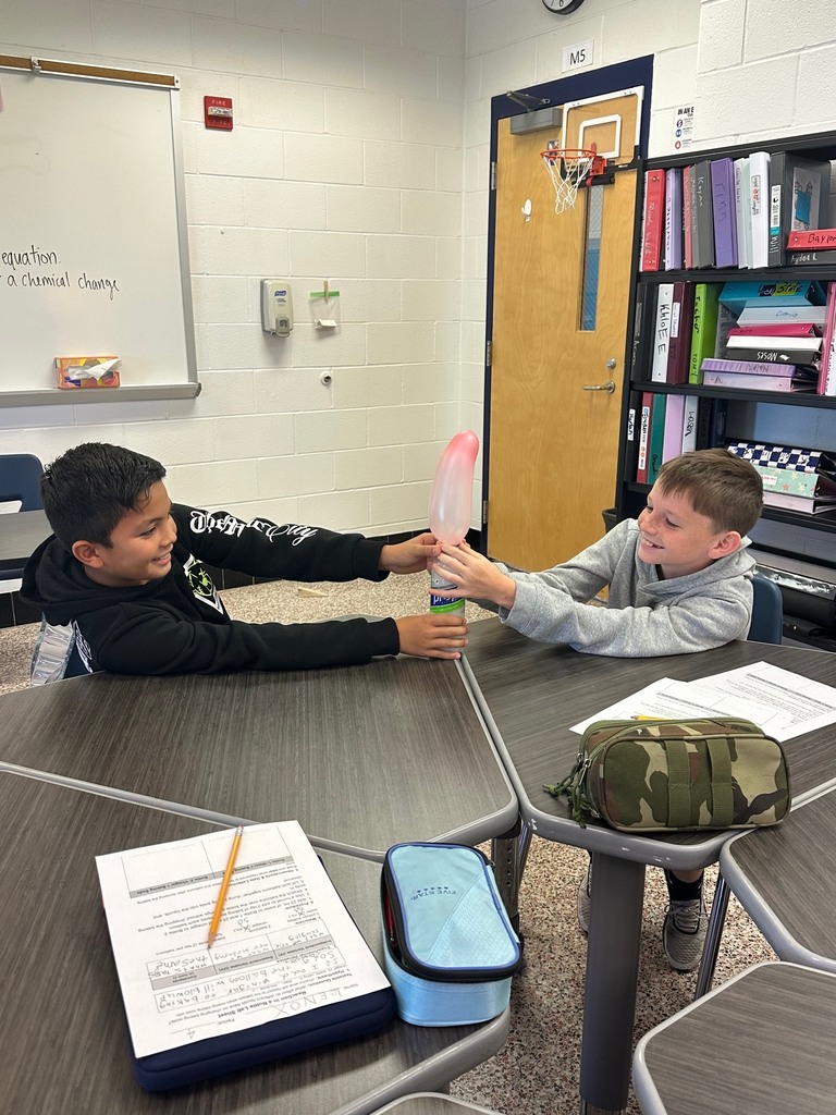 Two students work together during a science lab, observing a balloon inflate as a reaction occurs inside a bottle.