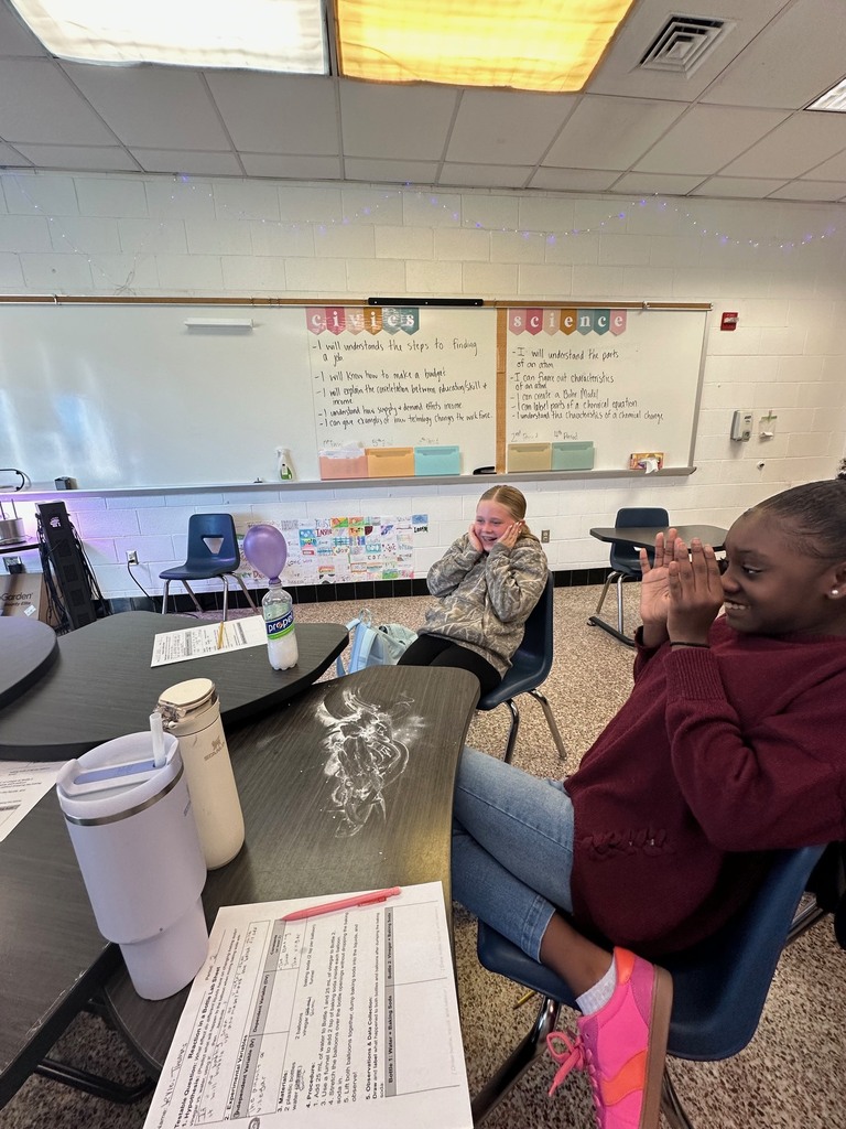 Students react with excitement as they observe the results of a chemical change experiment involving a balloon, bottle, and other materials.
