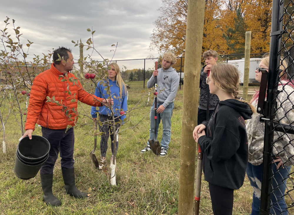 Teacher standing by sapling tree talking to students