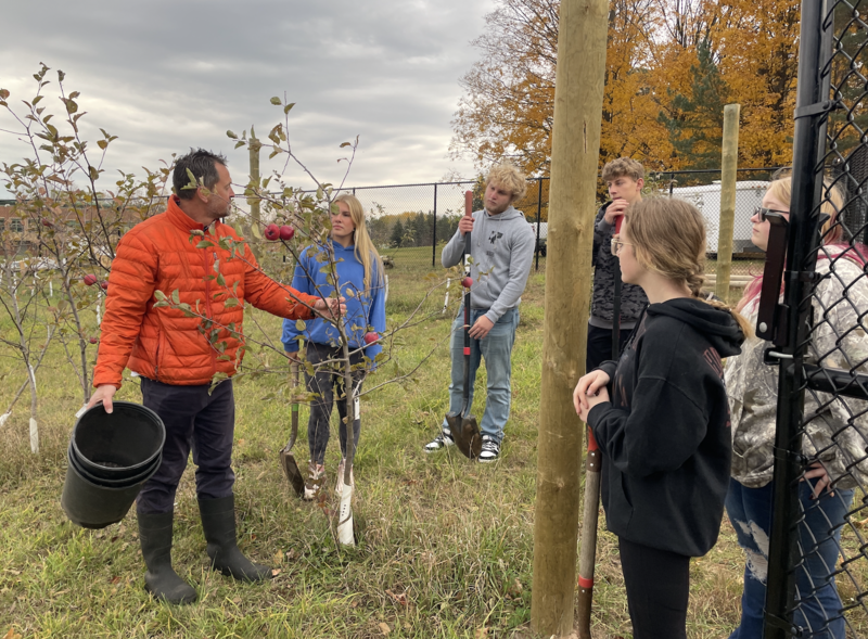 Teacher standing by sapling tree talking to students