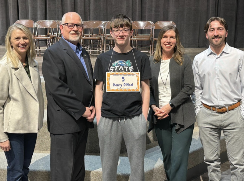 Student standing with adults with a name tag around his neck