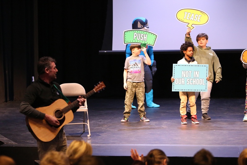 A person playing guitar with students on stage