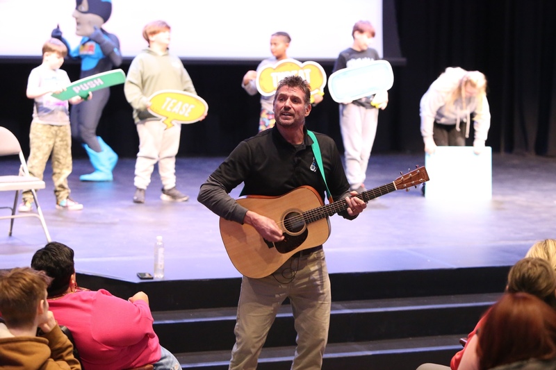 A person playing guitar with students on stage
