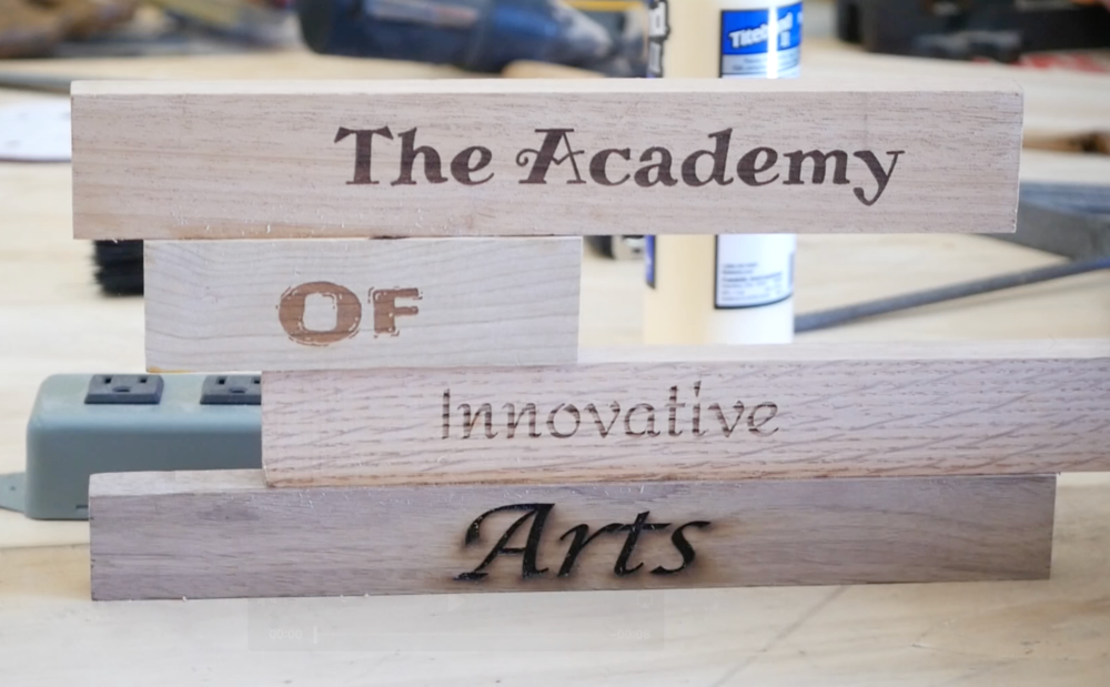 Wood laser cut with the words "The Academy of Innovative Arts"