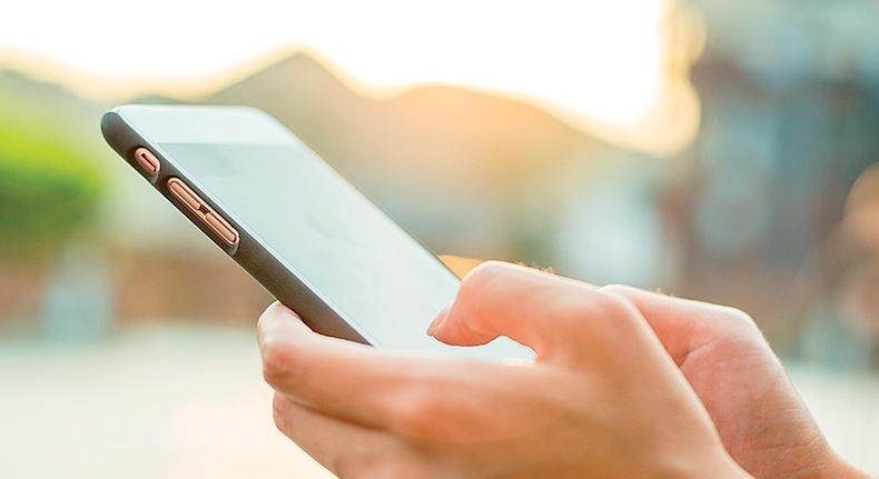 close up of hands typing on a smart phone with blurred background of the outdoors
