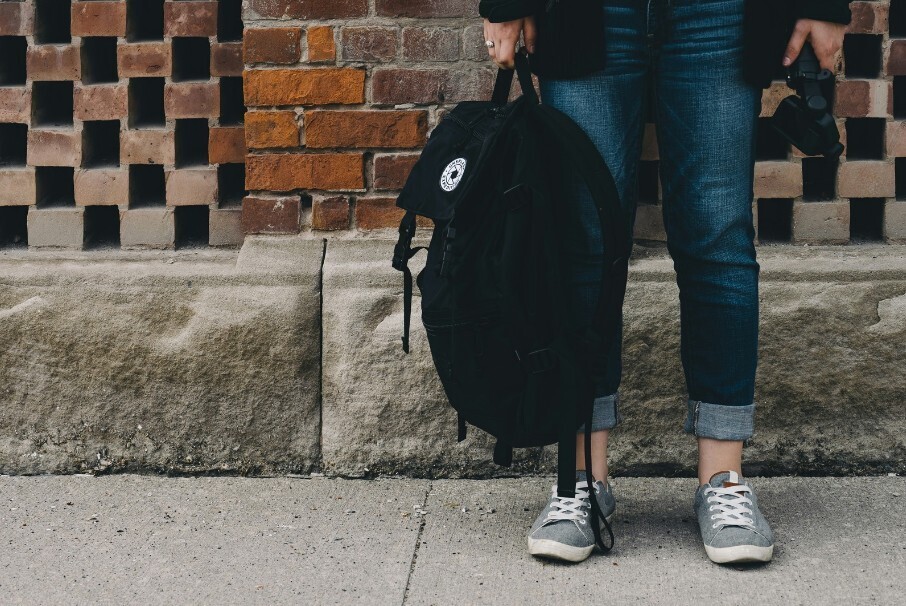 image of a student from the waist down standing up against a wall holding their backpack