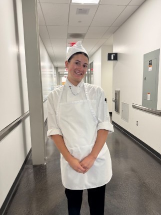 Grace standing in a hallway, posing in chef's whites