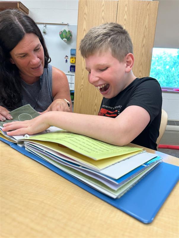 A female teacher assists a male student with a tactile book.
