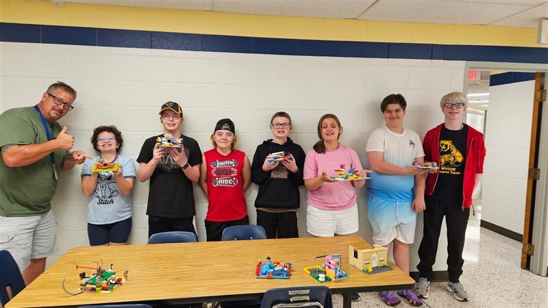 Students and a male RCS staff member stand side-by-side as they hold up their LEGO creations.