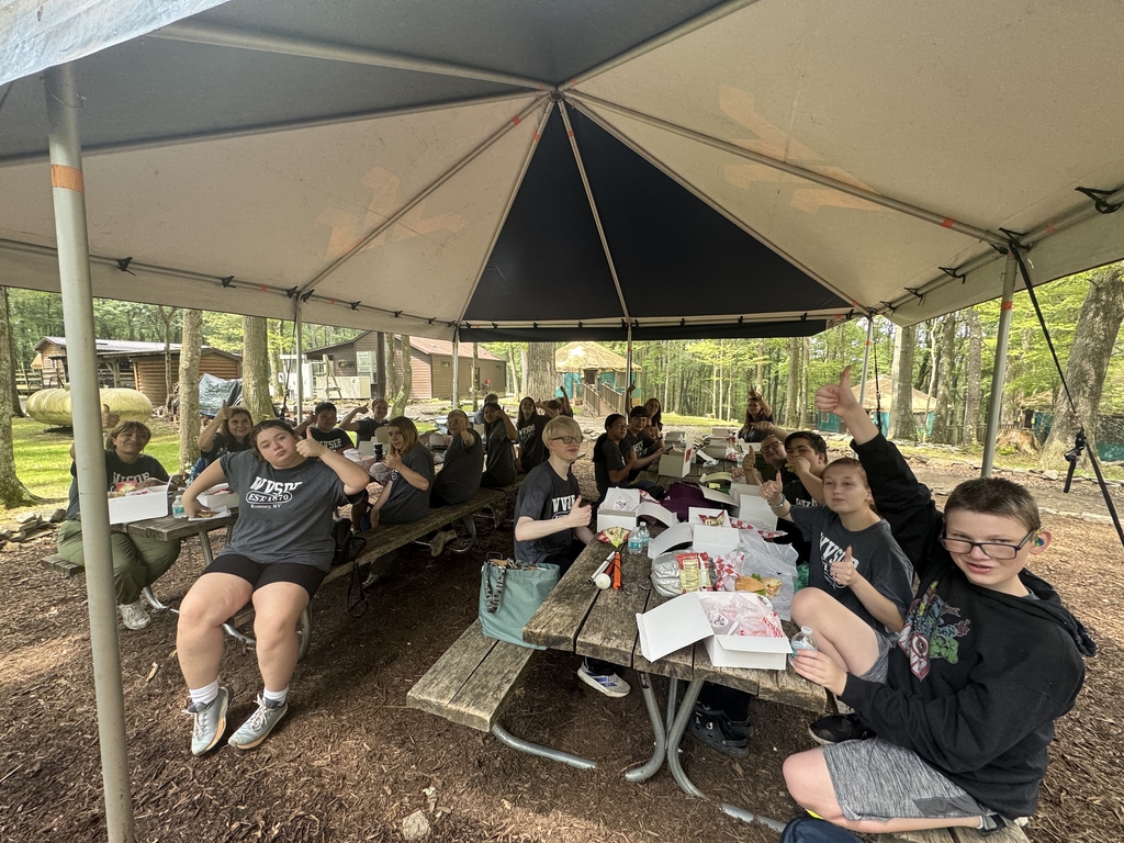 Camp participants seated at wooden picnic tables under a large tent enjoy their lunch.