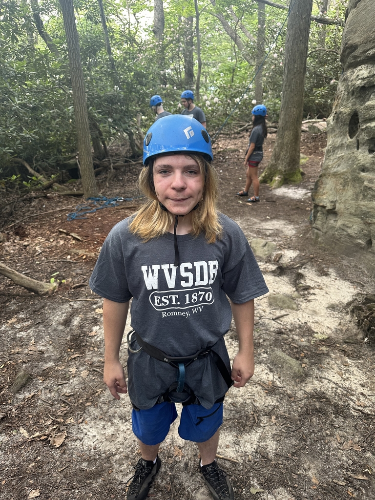 A male camp participant wearing a bright blue rock climbing helmet smiles for the camera.