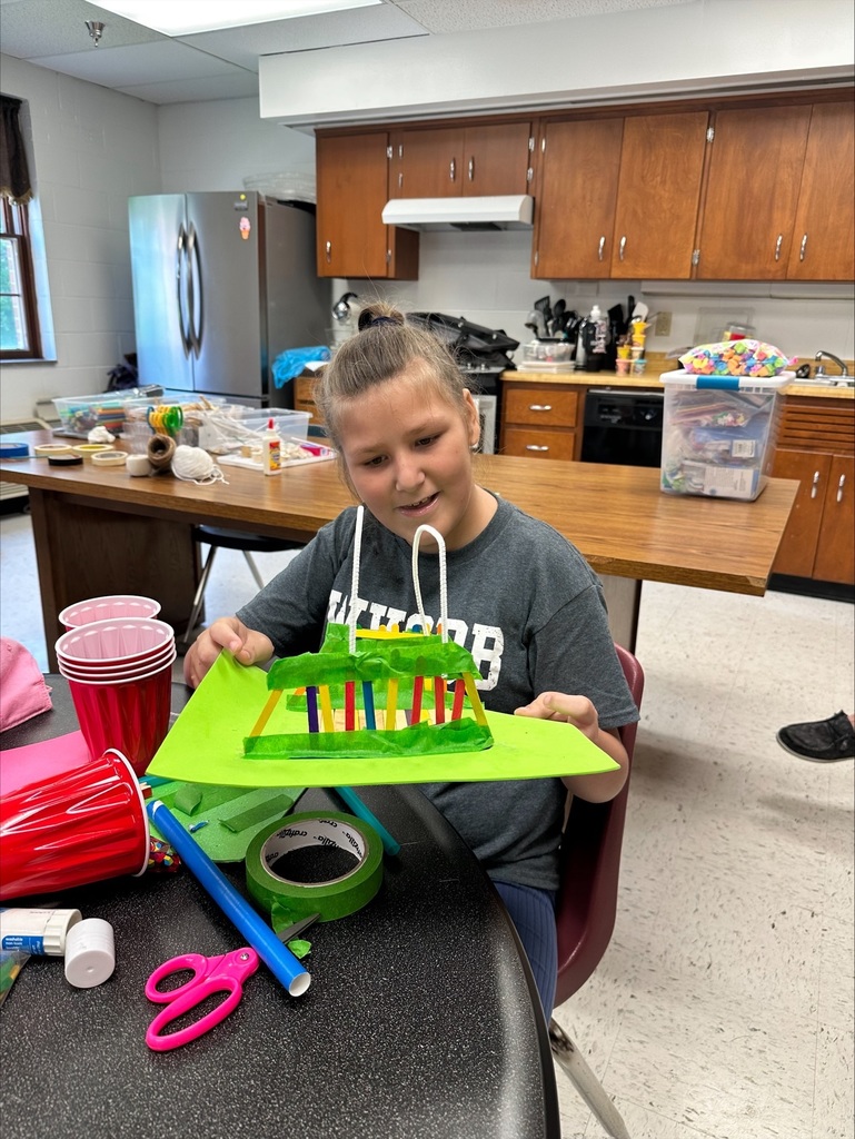 A female camp participant smiles as she looks down at her green-colored bridge creation.