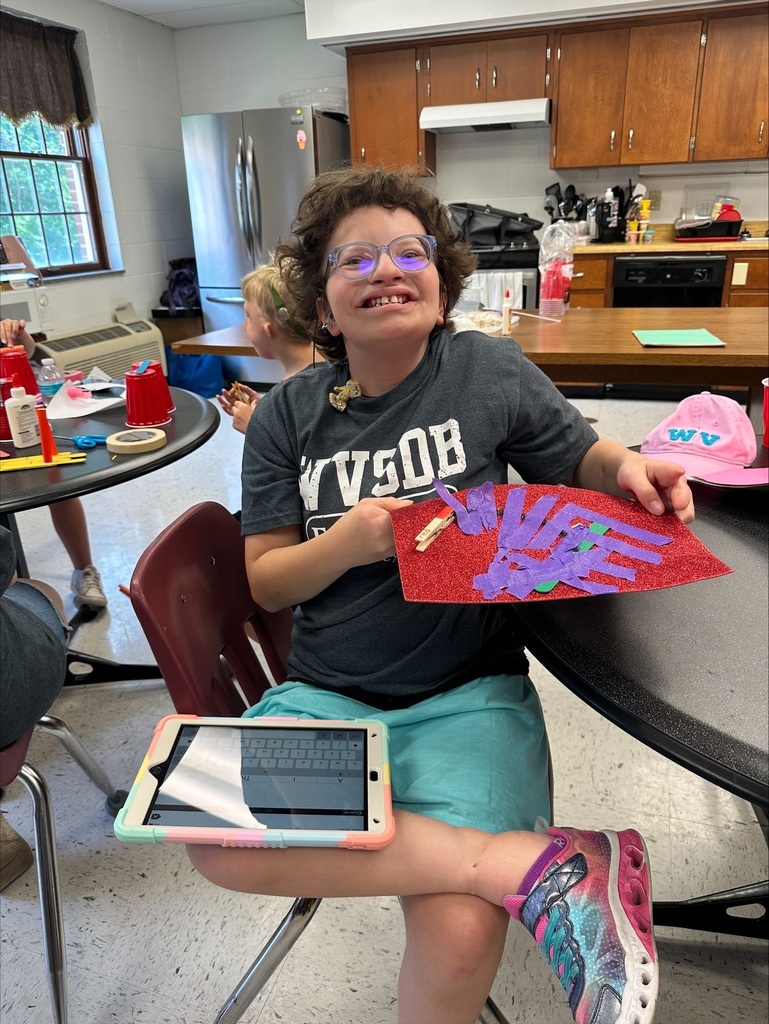 A camp participant holds up their bridge creation while smiling proudly at the camera.