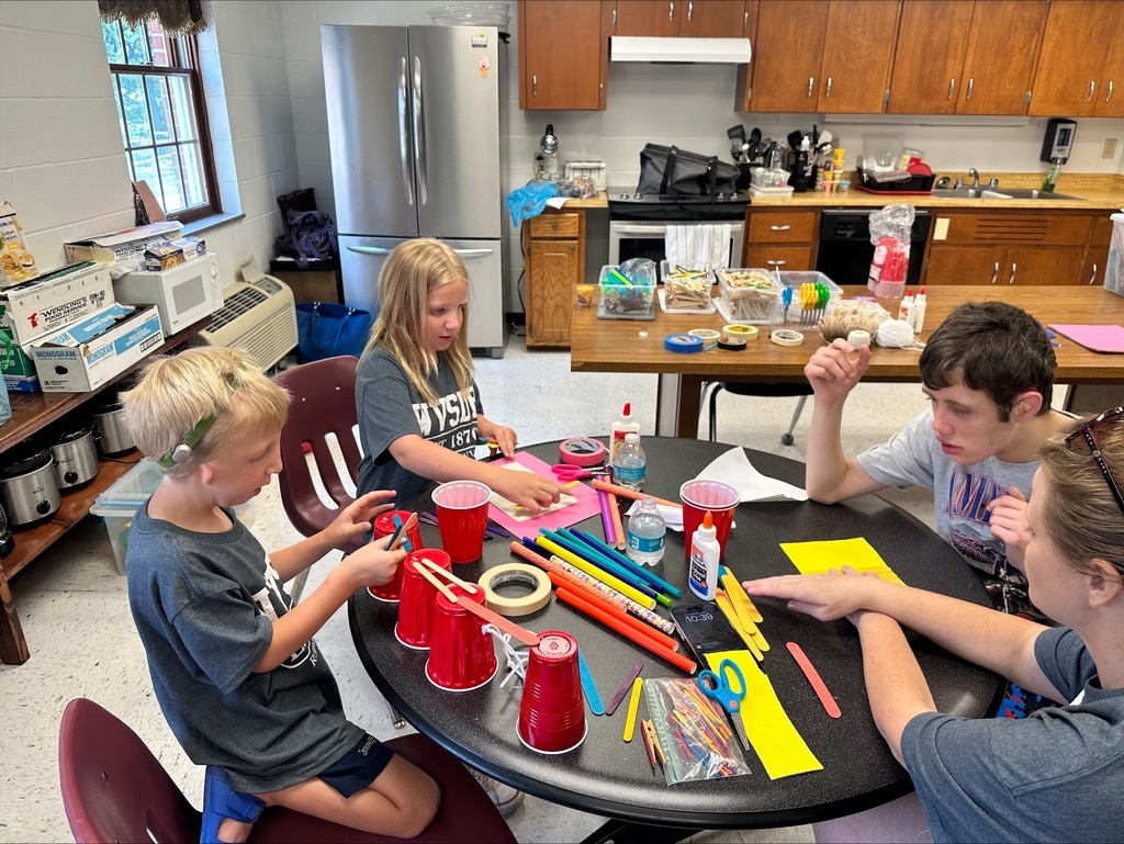 Camp participants are seated around a circular-shaped table while building their bridges.