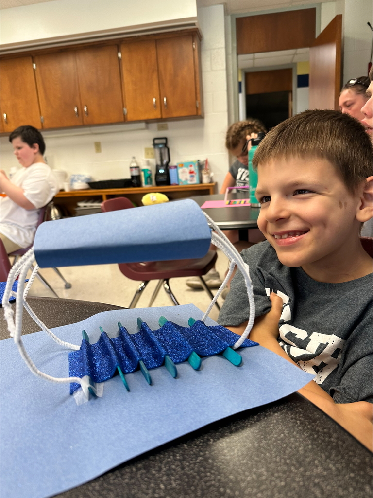 A male camp participant smiles at his blue-colored bridge creation.