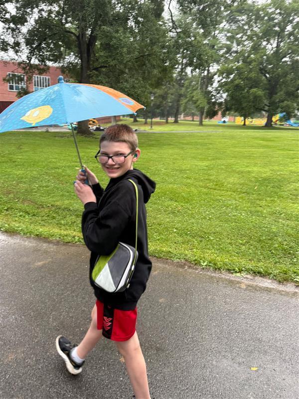A male camp participant smiles for the camera as he holds up a blue umbrella. 