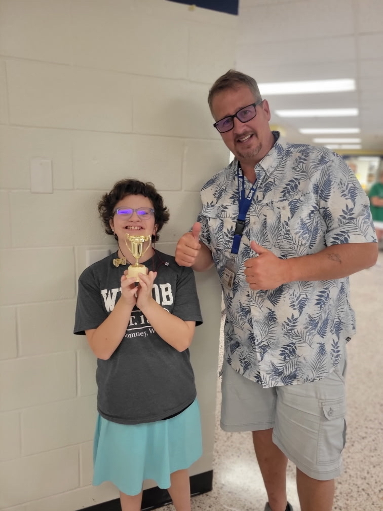 A male RCS staff member does a "thumbs up" with both his hands while a camp participant stands beside him holding up a small gold-colored trophy. 