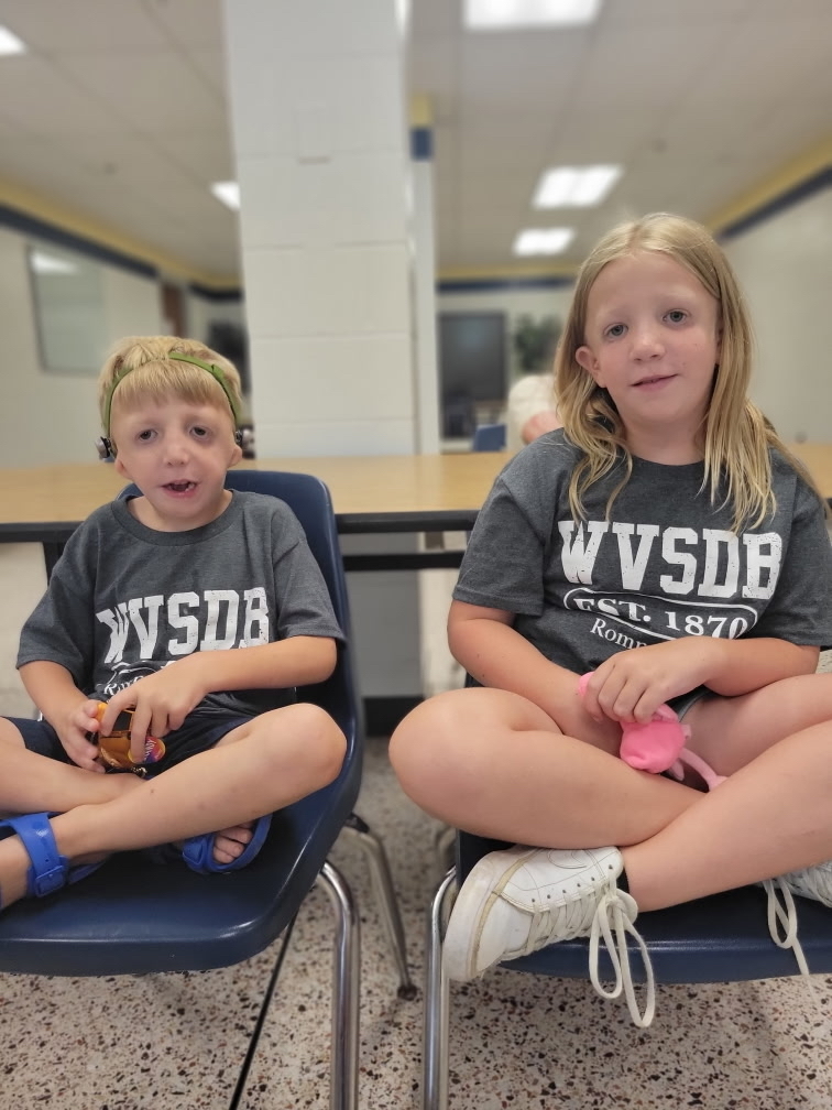 Two camp participants are seated in chairs, while they both smile at the camera. 
