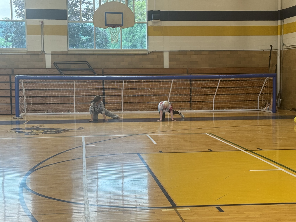 One female student demonstrates how to play goalball to a new camp participant in the gymnasium. 