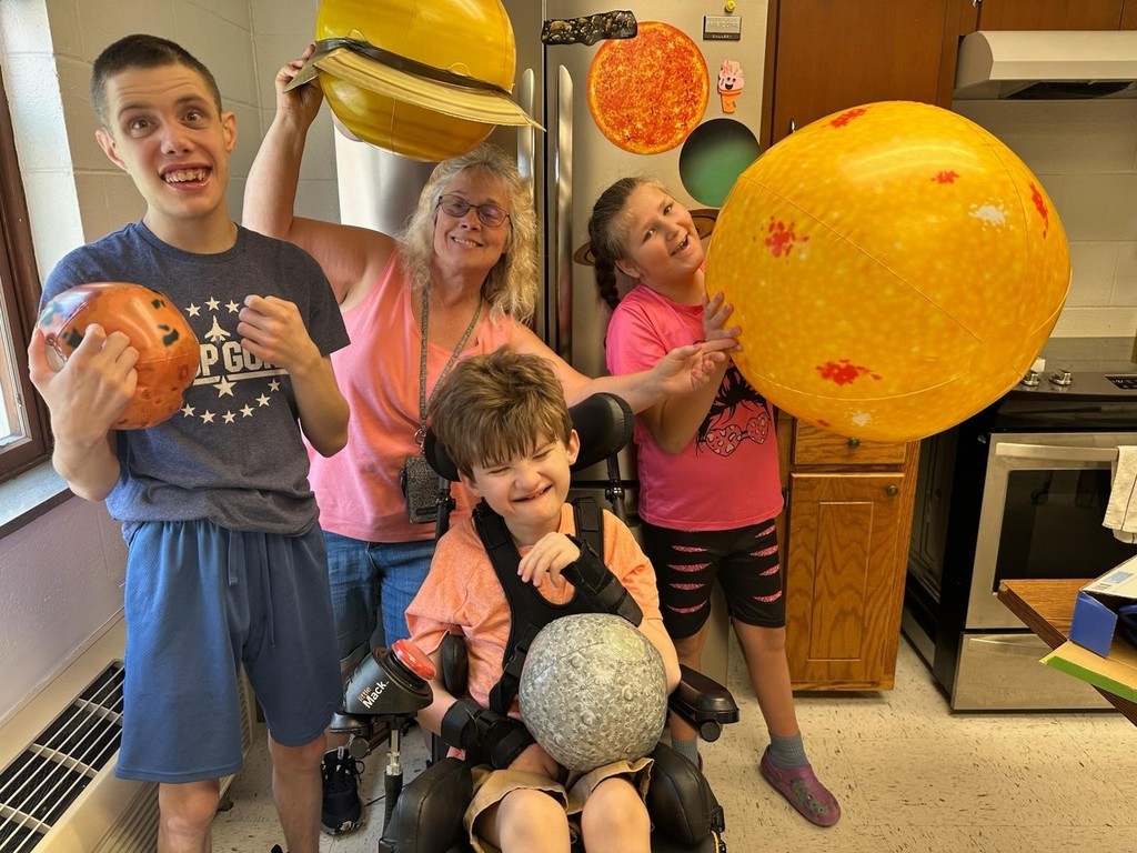 Camp participants stand close together as they hold up inflatable balls that represent the planets. 