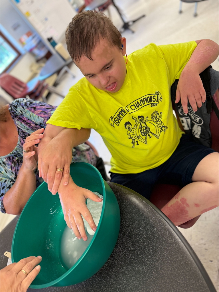 A male camp participant wearing a bright yellow shirt dips his hand in a green bowl filled with water.