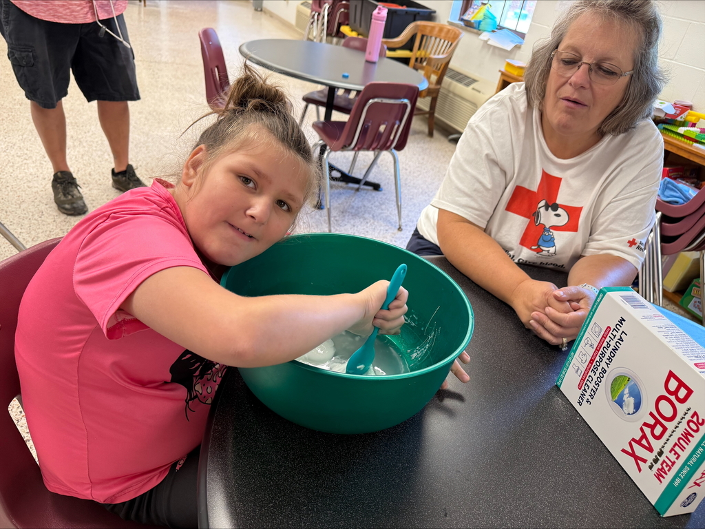 A female camp participant wearing a pink shirt is seated at a circular table as she stirs a mixture together in a green-colored bowl. 