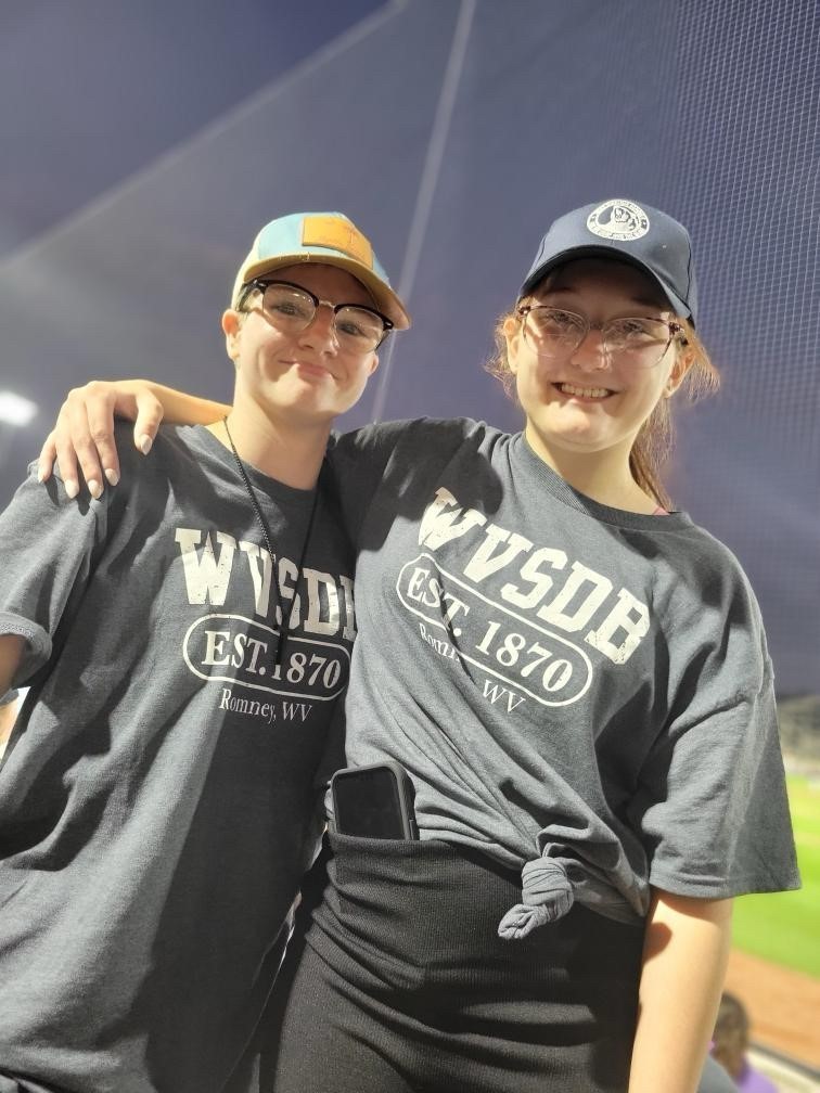 Two female camp participants wearing matching shirts stand side-by-side smiling for the camera. 
