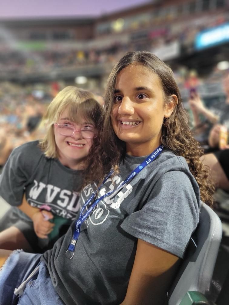 Two female camp participants seated in the stadium seats smile for the camera. 