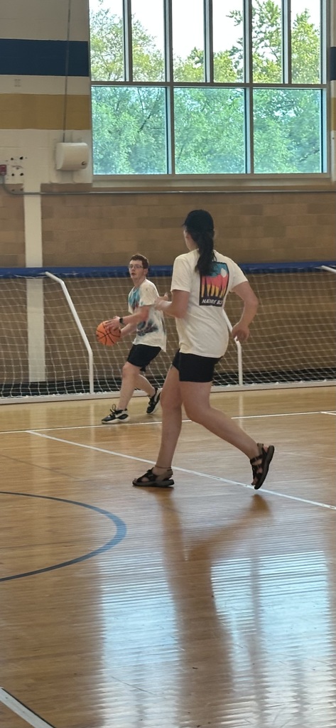 A male camp participant is dribbling an orange basketball in a gymnasium. 