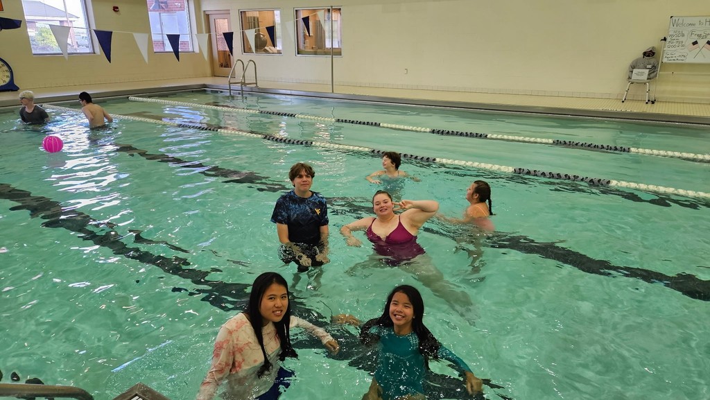 A group of camp participants are gathered around one another as they pose for the camera while they are standing in the shallow end of the pool. 