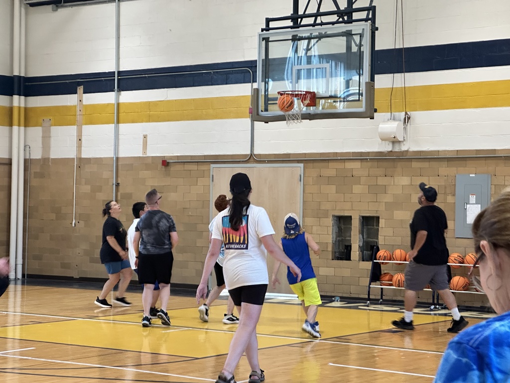 Camp participants shoot basketballs into the hoop inside of a gymnasium. 