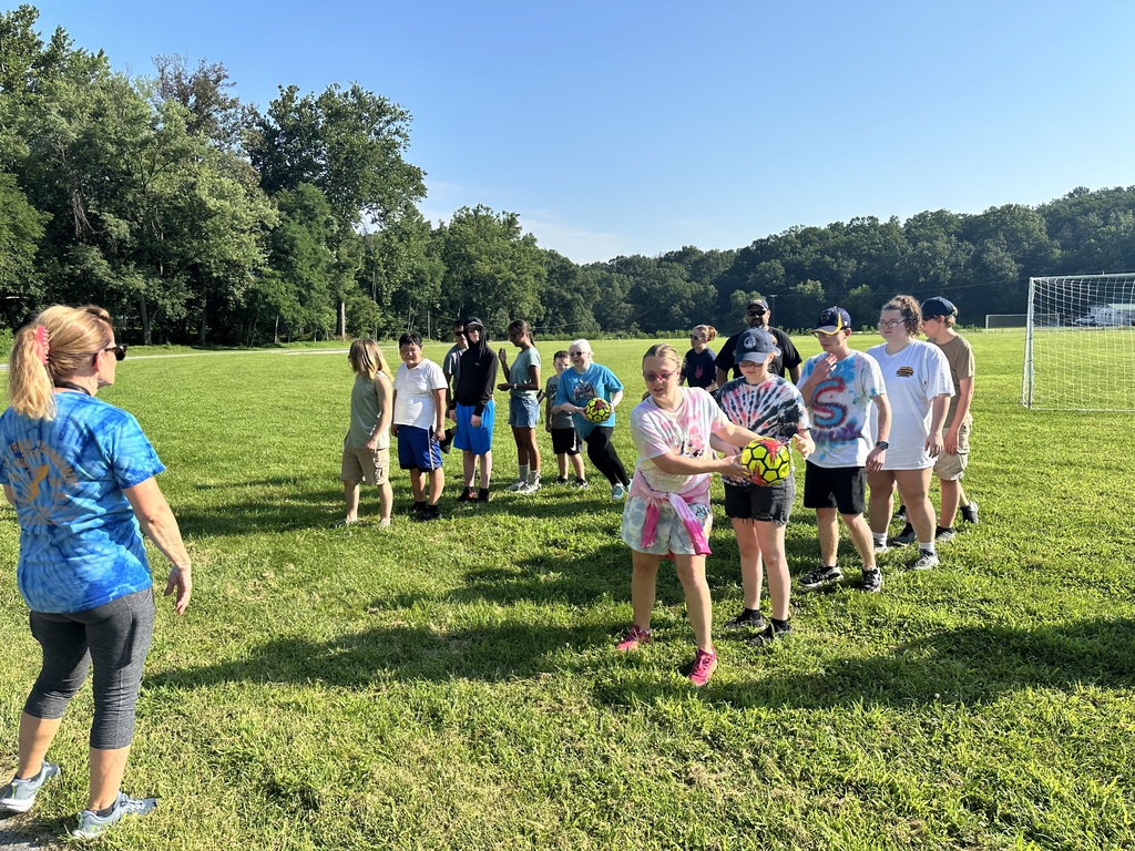 Camp participants are standing in two lines participating in an activity using a yellow and black ball. 