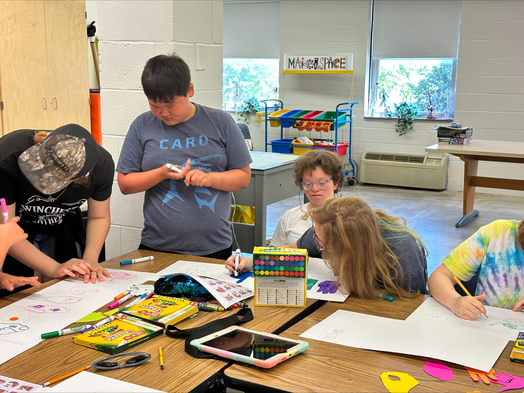 Camp participants are seated at a table as they using crayons, markers, and pencils to draw and color during an ASL activity. 