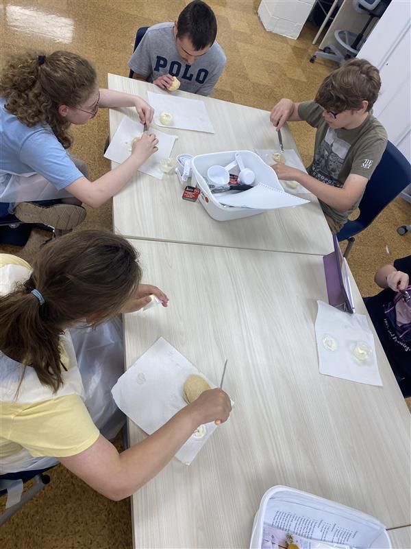 Camp participants seated around a light-colored table as they participate in an activity using dough.
