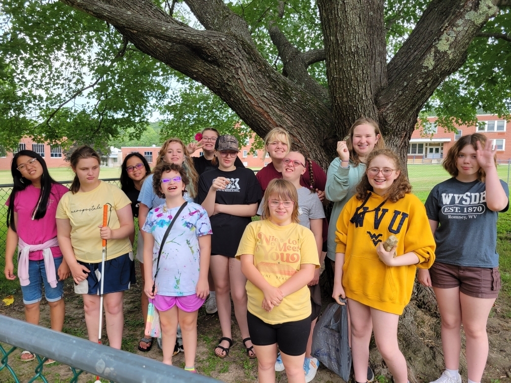 A group photo of camp participants standing side by side one another in front of a large tree.