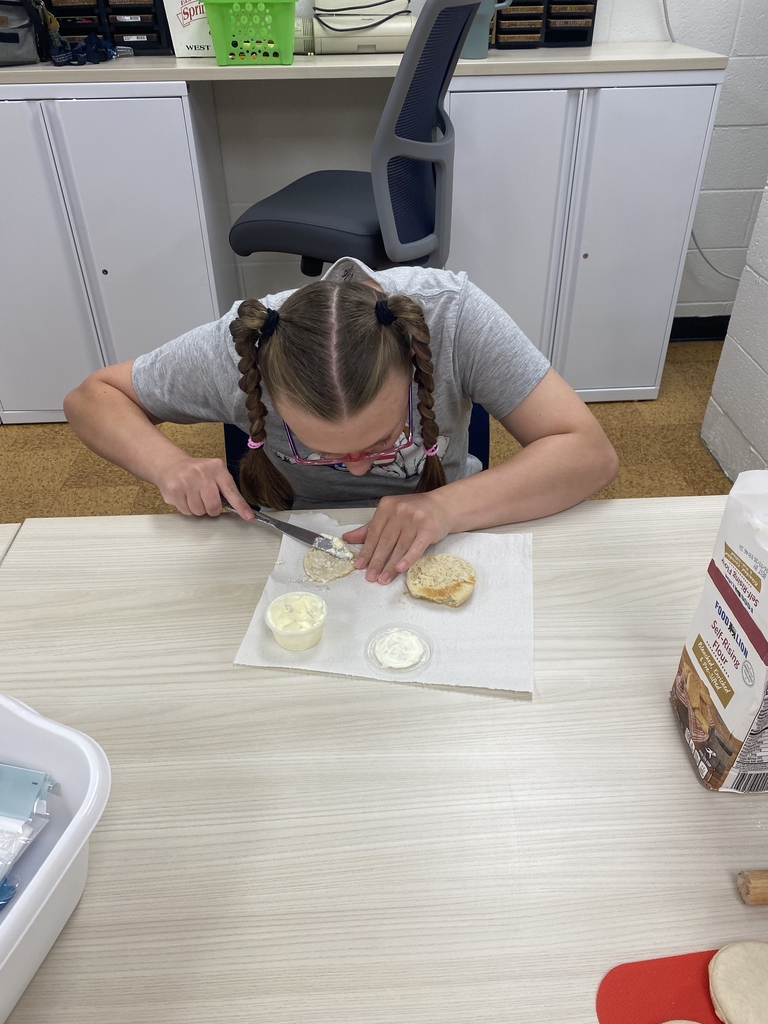 A female camp participant looks down as she focuses on buttering her bread that is sitting on top of a white-colored paper towel. 
