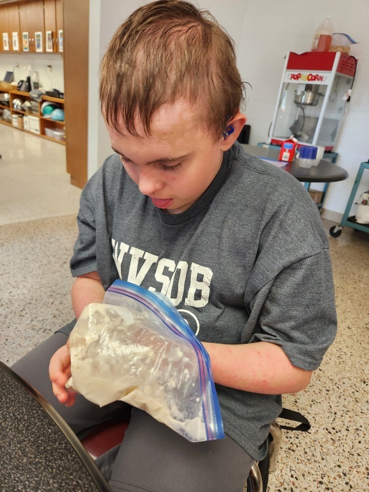 A male camp participant holds a bag full of beige-colored dough mixture. 