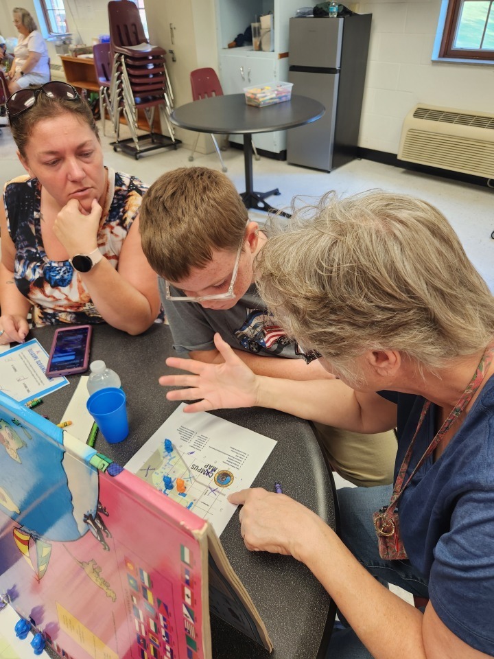 Two female aides assist a male camper with reading and understanding the WVSDB campus map. 