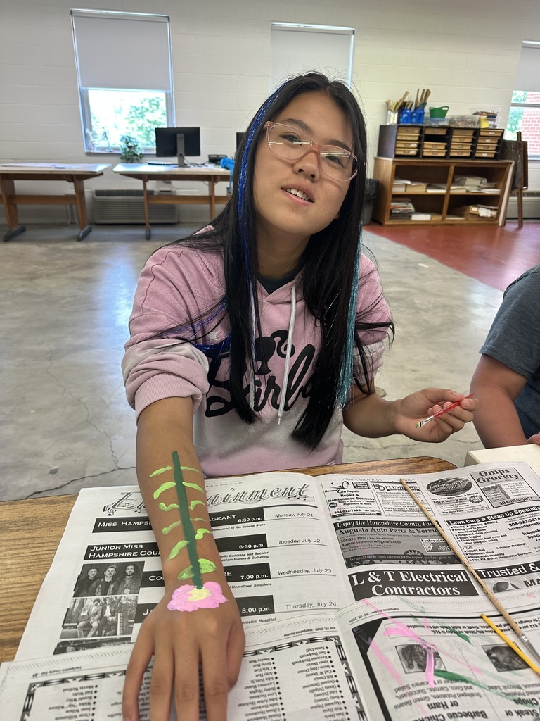 A female camp participant smiles for the camera as she holds out her arm that she painted a pink flower on during the ASL art activity.