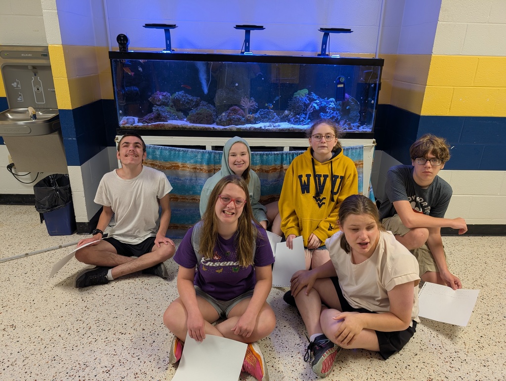 Group of Braille camp participants sitting in front of a large fish tank.