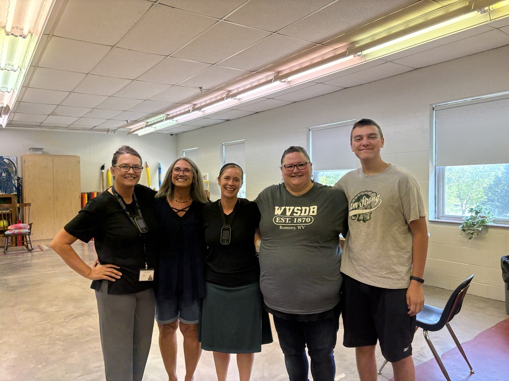 Group of ASL camp teachers, interpreters, aides, and volunteers stand together for a photo as they stand side by side one another. 
