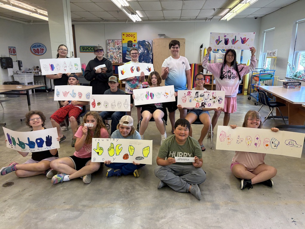 Group of ASL camp participants stand in a group, proudly holding up their art activities of ASL signs.