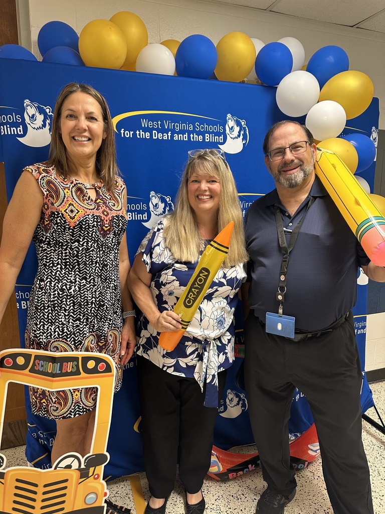 A group of three administrators stand in front of a blue backdrop, posing and smiling for the camera.