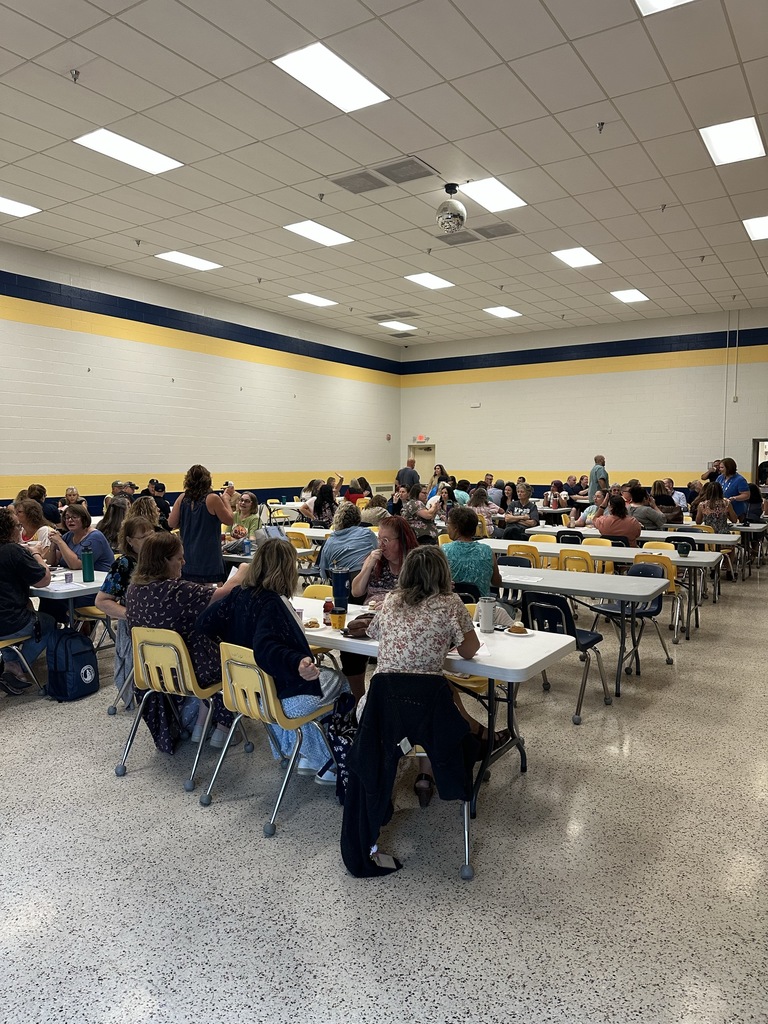 An overview of teachers and aides seated at tables as they participate in a meeting.