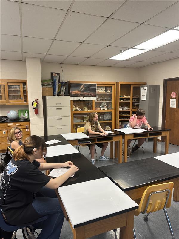 Students seated at their desks listening to their teacher.