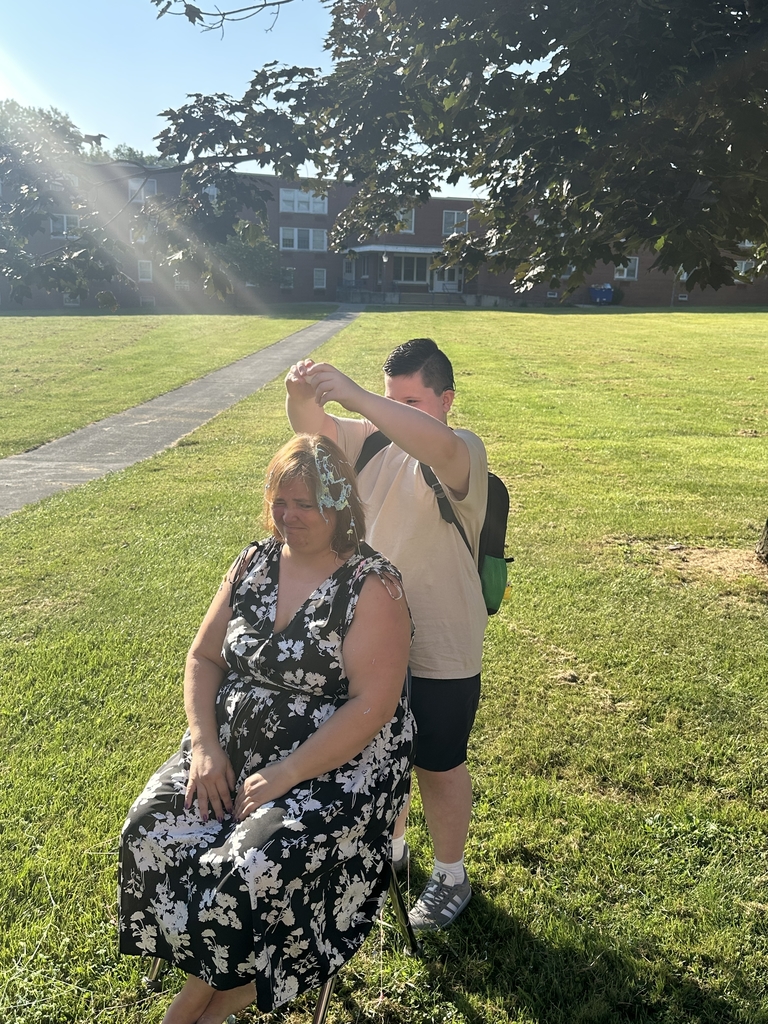 Mrs. Hesse sits in a chair as a male student cracks open an egg on her head.
