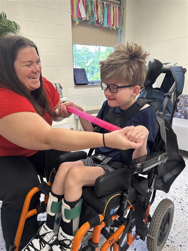Ms. Jasmine Morgan, Occupational Therapist helps a male student in a wheelchair use his hands to stretch a pink toy.