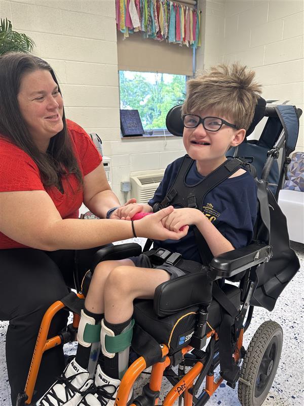 Ms. Jasmine Morgan, Occupational Therapist smiles while assisting a male student who is in a wheelchair.