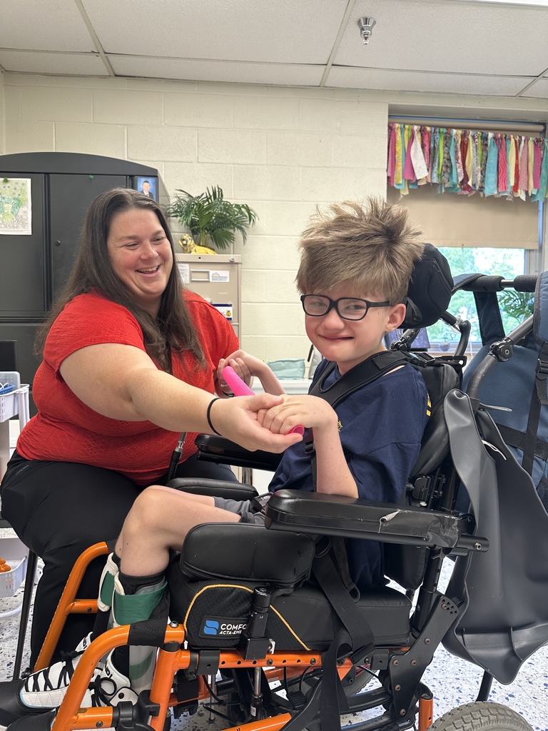 Ms. Jasmine Morgan, Occupational Therapist helps a male student in a wheelchair use his hands to stretch a pink toy.